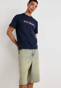 Jūras spēku kokvilnas T-krekls ar rozā krāsas "Pepe Jeans" logo, apvienots ar gaiši ziliem džinsa šortiem ar brīvu piegriezumu un piedurkņu malām.
