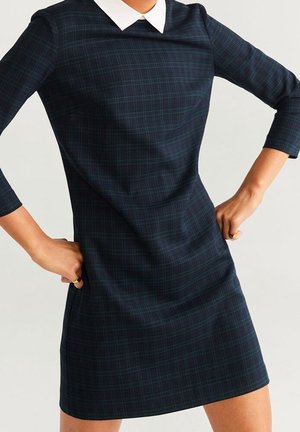 Robe à carreaux marine avec un col blanc, des manches trois-quarts, un buste ajusté et une jupe évasée. Tissu lisse avec une texture subtile.