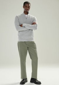 Suéter de cuello con cremallera color gris claro con textura acanalada, combinado con pantalones verde oliva. El modelo lleva zapatos negros de punta redonda y cordones.
