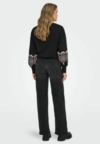 �Črna dukserica z vzorčastimi, vezenimi rokavi, v kombinaciji z visokim pasom, temnimi jeans hlačami in debelimi črnimi čevlji.