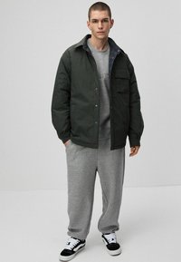 Zielona pikowana kurtka z kieszenią z przodu, szara bluza pod spodem i szare dresy. Czarno-białe sneakersy dopełniają outfit.