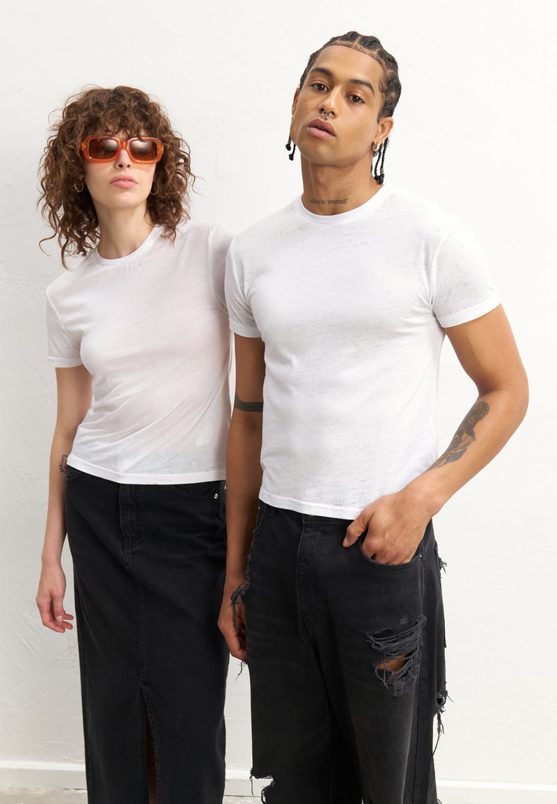 T-shirts brancos, ajustados, de manga curta em tecido leve, combinados com jeans pretos e uma saia longa, exibindo um look casual e em camadas.