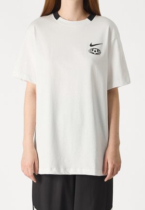 White oversized short-sleeve t-shirt with black Nike logo and soccer ball graphic on the left chest, worn by a person with long hair.