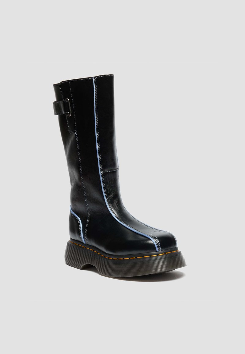 Tall black leather boot with chunky sole, light blue stitching accents, and a strap with buckle near the top.