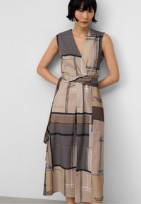 Robe portefeuille sans manches en tissu texturé présentant un motif géométrique avec des tons terreux, notamment beige, marron et gris.