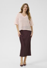 Pull court en tricot léger rose pâle à manches courtes avec un col en V, associé à une longue jupe en satin bordeaux et des escarpins à bout pointu.