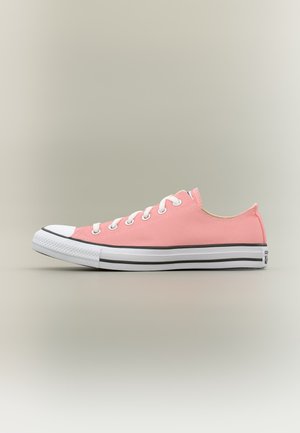 Niedriger pinker Canvas-Sneaker mit weißer Gummikappe an der Spitze, weißen Schnürsenkeln und weißer Sohle mit schwarzen Streifen auf neutralem Hintergrund.
