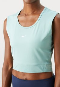 Svijetloplava, bez rukava, atletska crop majica od glatkog materijala, s okruglim izrezom i malim bijelim Nike logom sprijeda.