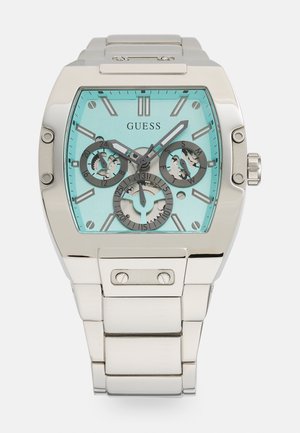 Montre-bracelet Guess en métal argenté avec un cadran rectangulaire turquoise, trois sous-cadrans pour les fonctions 24 heures, jour et date.