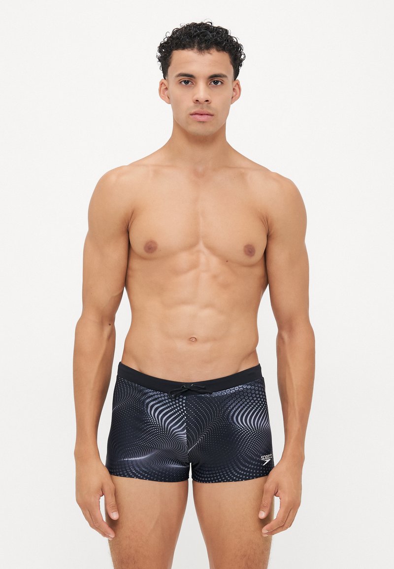 Schwarze Badeshorts mit einem wirbelnden, gepunkteten Muster. Hergestellt aus glattem, dehnbarem Material mit einem schwarzen Bund und verstellbarem Kordelzug.