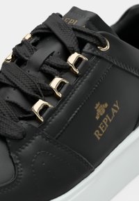 Czarny skórzany sneaker z grubymi czarnymi sznurówkami, złotymi hakami na sznurówki, logo "REPLAY" i białą podeszwą w zbliżeniu.
