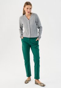 Světle šedý pletený kardigan s výstřihem do V a čtyřmi knoflíky, doplněný o zelené kalhoty v slim fit a baleríny s hadím vzorem.