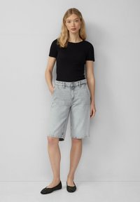 Zwarte ribbelige top met korte mouwen, gecombineerd met lichtgewassen denim Bermuda-shorts en zwarte ballerina's, wat een casual outfit laat zien.