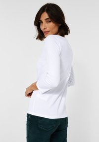 Witte blouse met lange mouwen en een ronde halslijn, gemaakt van zacht katoen met een relaxte pasvorm; gedragen met donkergroene broek, die een eenvoudig ontwerp toont.