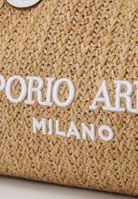 Sac en paille tressée beige avec le texte brodé en blanc "EMPORIO ARMANI MILANO", présentant un design texturé et naturel avec un haut arrondi.