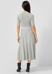 Graues, geripptes Strickkleid mit tailliertem Oberteil und ausgestelltem, knielangem Rock. Es hat kurze Ärmel und einen Taillengürtel, kombiniert mit schwarzen Knöchelstiefeln.