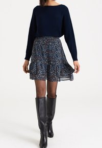 Granatowy sweter z dzianiny w połączeniu z warstwową spódnicą w ciemne kwiatowe wzory. Nosi się go z czarnymi skórzanymi botkami do kolan.