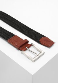 Zwarte geweven riem met bruine leren accenten en een zilveren metalen gesp. Beschikt over een gestructureerde stof en slanke platte uiteinden.