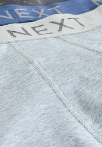 Boxeri scurți din bumbac de culoare albastru deschis, cu un brâu elastic gri pe care este inscripționat textul "NEXT" în gri închis. Cusăturile sunt vizibile de-a lungul cusăturilor.