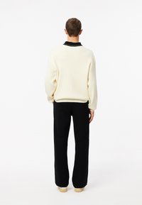 Suéter de canalé crema con un cuello negro, combinado con pantalones negros de pierna ancha. El conjunto tiene un corte relajado y una textura de tela suave.