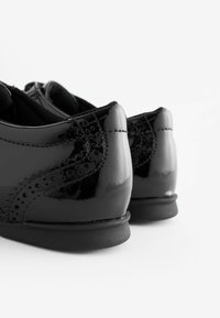 Schwarze Lackleder Schuhe mit dekorativen Perforationen und einer glatten, glänzenden Oberfläche. Flache Sohle mit abgerundetem Absatz.