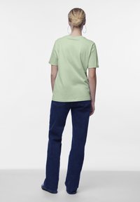 T-shirt verde chiaro a maniche corte con vestibilità rilassata, abbinata a jeans a zampa d'elefante blu scuro. Tessuto in cotone morbido, design semplice, senza grafiche visibili.