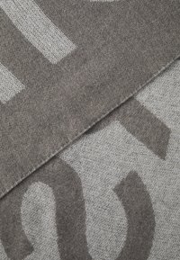 Tessuto grigio con grandi motivi audaci in grigio chiaro. Il tessuto ha una texture morbida con un aspetto intrecciato, mostrando sezioni sovrapposte.