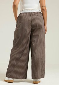 Bruna randiga vida byxor med vit elastisk midja, gjorda av slät tyg, med vertikala ränder och sidofickor.