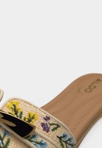 Sandale à glissière couleur fauve avec des brides à imprimé floral tissé en jaune, violet et bleu, ornée d'une boucle décorative noire et dorée.