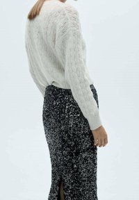 Sweter wykonany z bawełnianego splotu w kolorze kości słoniowej o luźnym fasonie, zestawiony z czarną spódnicą z cekinami z bocznym rozcięciem. Gładka tekstura i błyszczące akcenty.