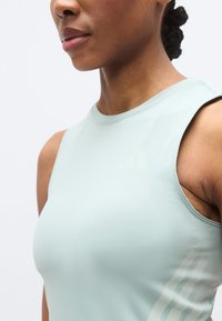 Haut de sport sans manches de couleur bleu sarcelle clair, réalisé en tissu extensible, avec un col rond et un détail discret à rayures sur le côté.