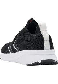 Svart sportskon med ett strukturerat stickat övre, vit sula och en kontrasterande vit dragflik. Har svarta accenter på sidan.