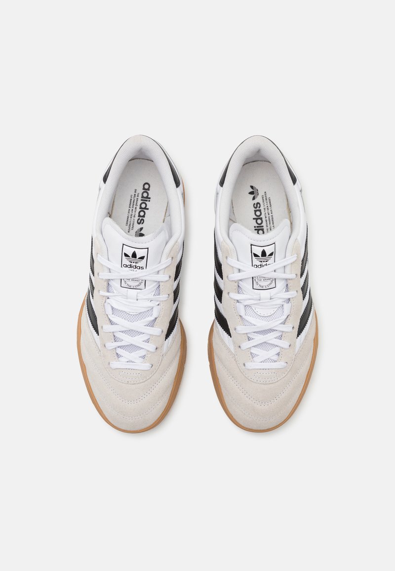 Weiße und beige Sport Schuhe mit schwarzen Streifen, aus Wildleder und Netzmaterial, flachen Schnürsenkeln und Gummisohle. Mit Branding auf der Zunge.