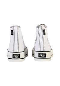 Zapatillas altas blancas con costuras negras, suelas de goma y etiquetas de marca en ambos lados del talón. Diseño simple sin patrones distintivos.
