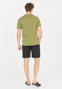 Olivgrön bomullströja med korta ärmar, kombinerad med svarta shorts. Enkel design, avslappnad passform, minimal detaljer och platt textur.