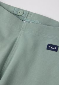 Lichtgroene broek met een gladde textuur, voorzien van een knoopsluiting en een klein marineblauw label met de tekst "P.O.P." op de taille.