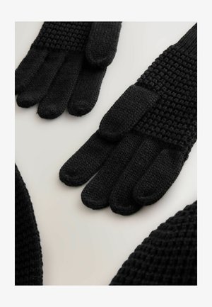 Gants en tricot noirs avec un dessus texturé, des doigts lisses et des pointes arrondies. Présentent un motif côtelé et un poignet élastique pour un ajustement confortable.