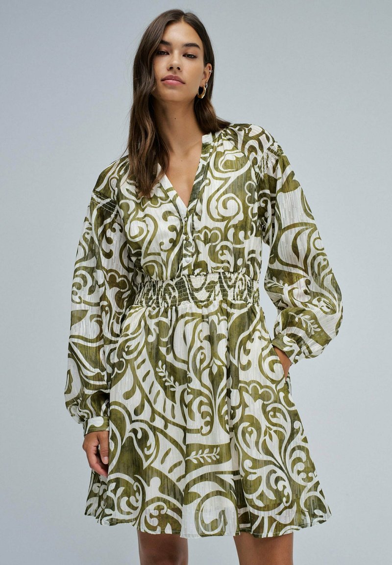 Vestido verde y blanco con estampado, cuello en V, mangas largas, cinturilla elástica y bolsillos; tejido ligero con un acabado texturizado.