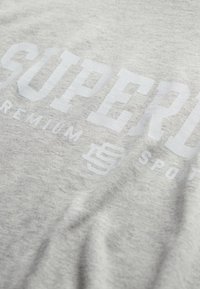 Grå bomulds t-shirt med stor hvid tekst, der læser "SUPERB" og "PREMIUM SPORTS", med en glat tekstur og afslappet pasform.