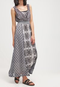 Maxi sukienka z dopasowanym gorsetem i luźną spódnicą, w czarno-białe wzory, z przezroczystymi nakładkami i lekkim materiałem. Sandały z odkrytymi palcami.