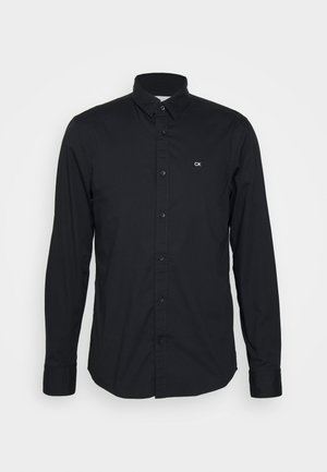 Black long-sleeve shirt made of cotton with a button-down collar, featuring a small CK logo on the left chest and a straight hem.