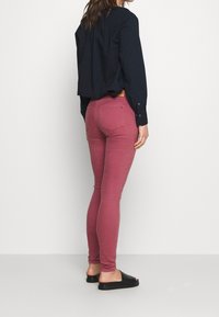 Skräddarsydda mörkrosa jeans med en slät textur, tillsammans med en svart långärmad topp och svarta slip-on sandaler. Synliga bakfickor.