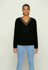 Top preto de manga longa com decote em V e acabamento em renda; textura suave, corte descontraído, combinado com jeans justos de tom azul claro.