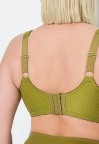 Olivgrön bh med texturerad tyg, justerbara remmar och hakhake-lås bak. Cirkulära metallaccenter.