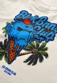 Witte T-shirt met een kleurraf grafiek van een blauwe ijscocone met een aap gezicht, die druipt van de verf en omringd is door palmbomen.