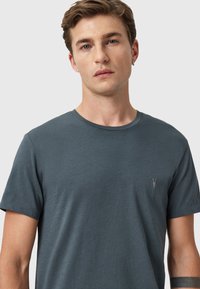 Camiseta de manga corta en gris oscuro, fabricada con tejido suave. Cuenta con un cuello redondo y un pequeño logo bordado en el pecho. Textura suave.