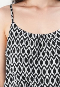 Débardeur à motifs noir et blanc présentant un design en forme de losange, des bretelles sans manches, et une coupe décontractée avec un tissu doux et texturé.