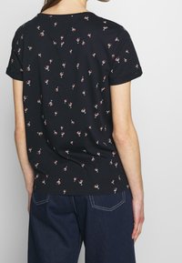 T-shirt noir à manches courtes avec un motif répétitif de cocktails. Le matériau semble doux ; l'encolure est ronde. Design décontracté adapté à un usage quotidien.