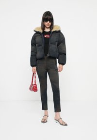 Black puffer jacket with faux fur collar, fitted black top, dark patterned jeans, and red handbag. Model wears sunglasses and strappy heels.