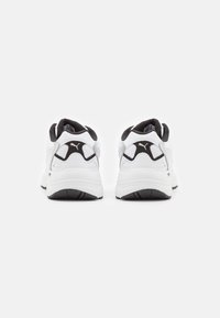 Chaussures de sport blanches avec des accents noirs, col rembourré, matériau texturé et détail du logo sur le talon. Semelle extérieure en caoutchouc solide.